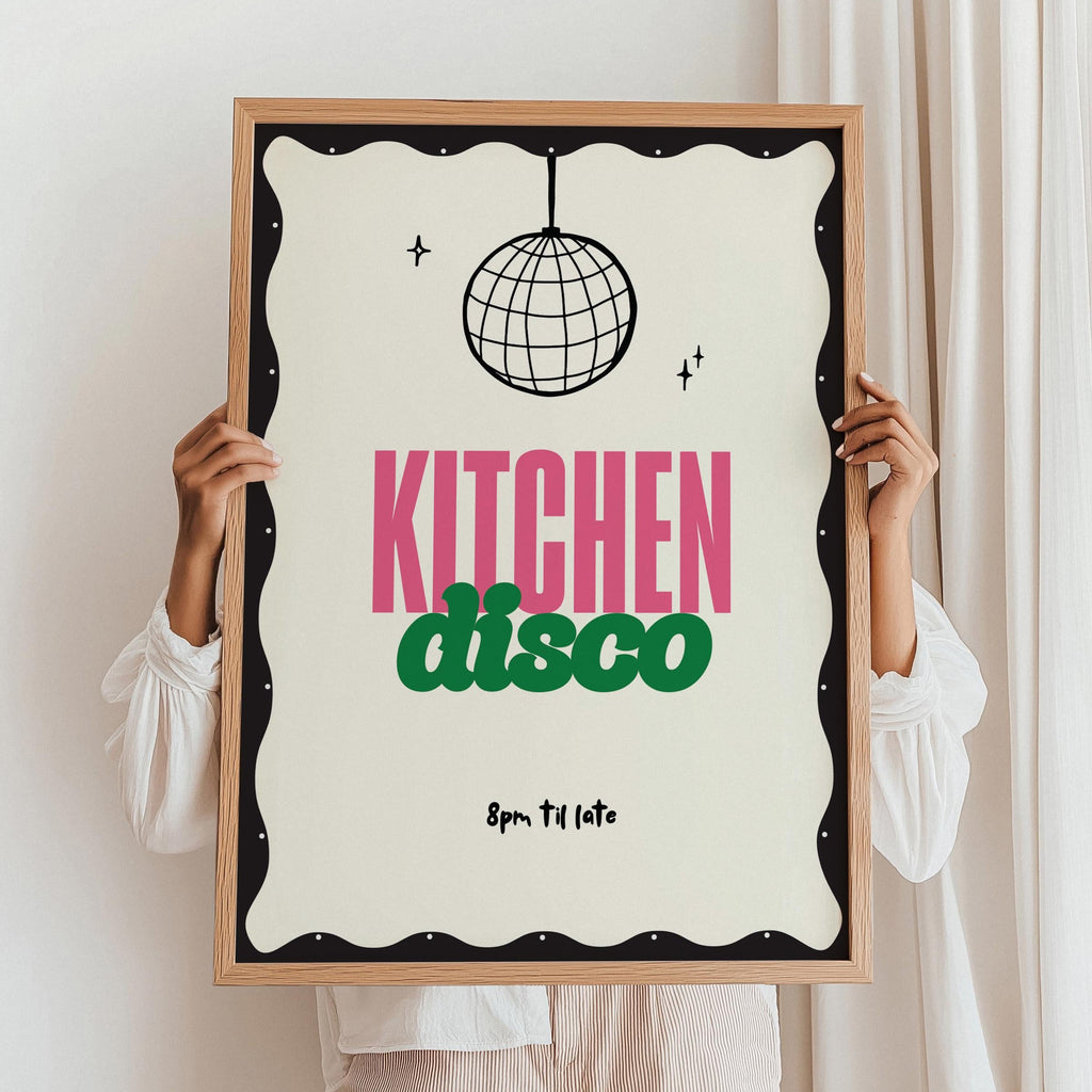 Person holding a framed poster with 'Kitchen Disco' text and disco ball design.