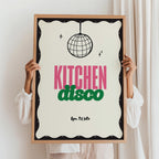 Person holding a framed poster with 'Kitchen Disco' text and disco ball design.