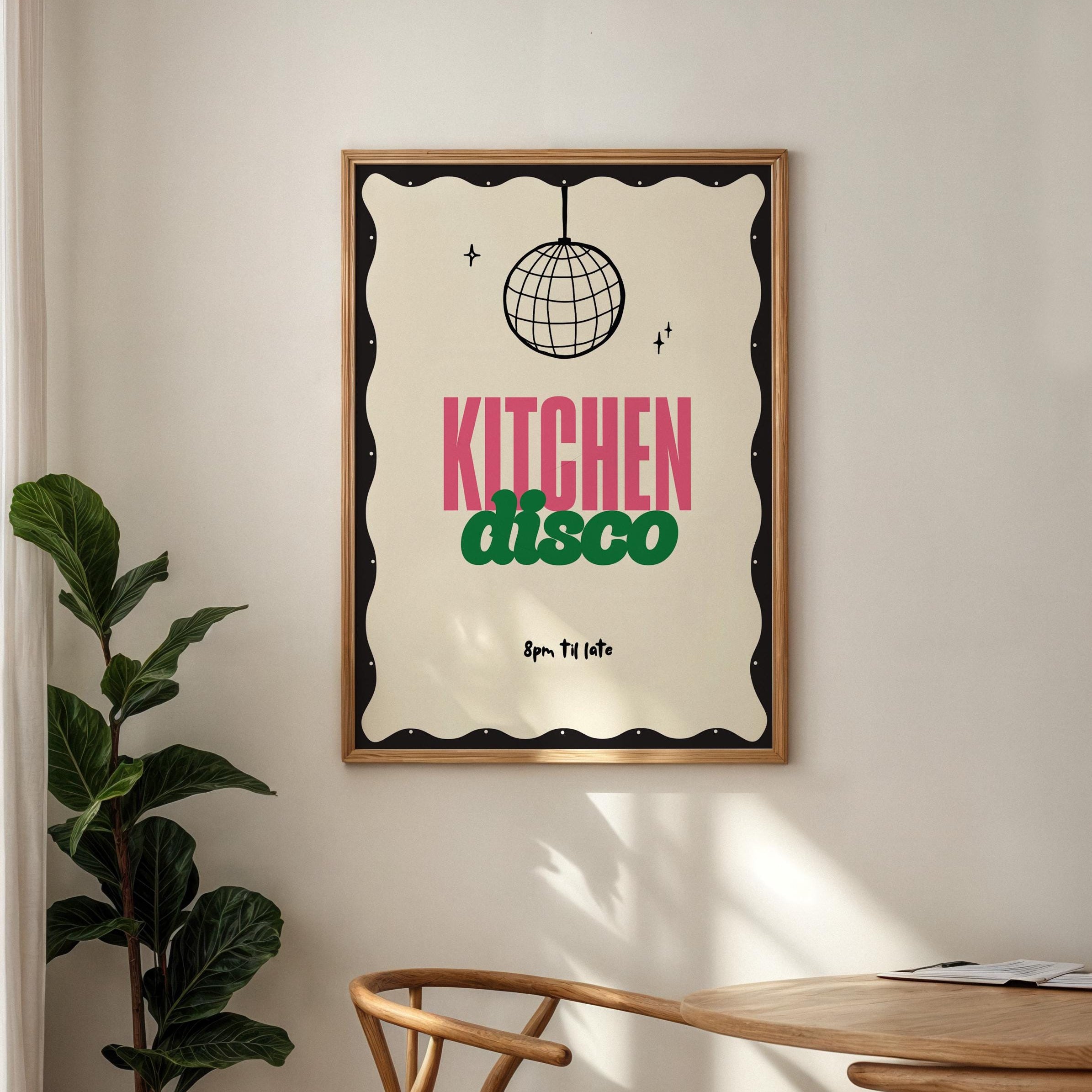 Framed 'Kitchen Disco' poster on a wall above a wooden chair and table.