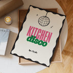 Decorative sign with 'Kitchen Disco' text on a table with a cup of coffee and books.