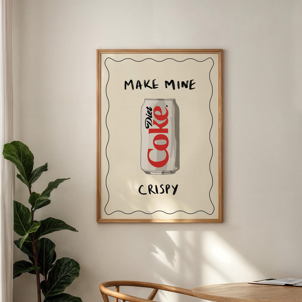 Framed artwork with Diet Coke can design on a wall with a plant and table in the foreground.