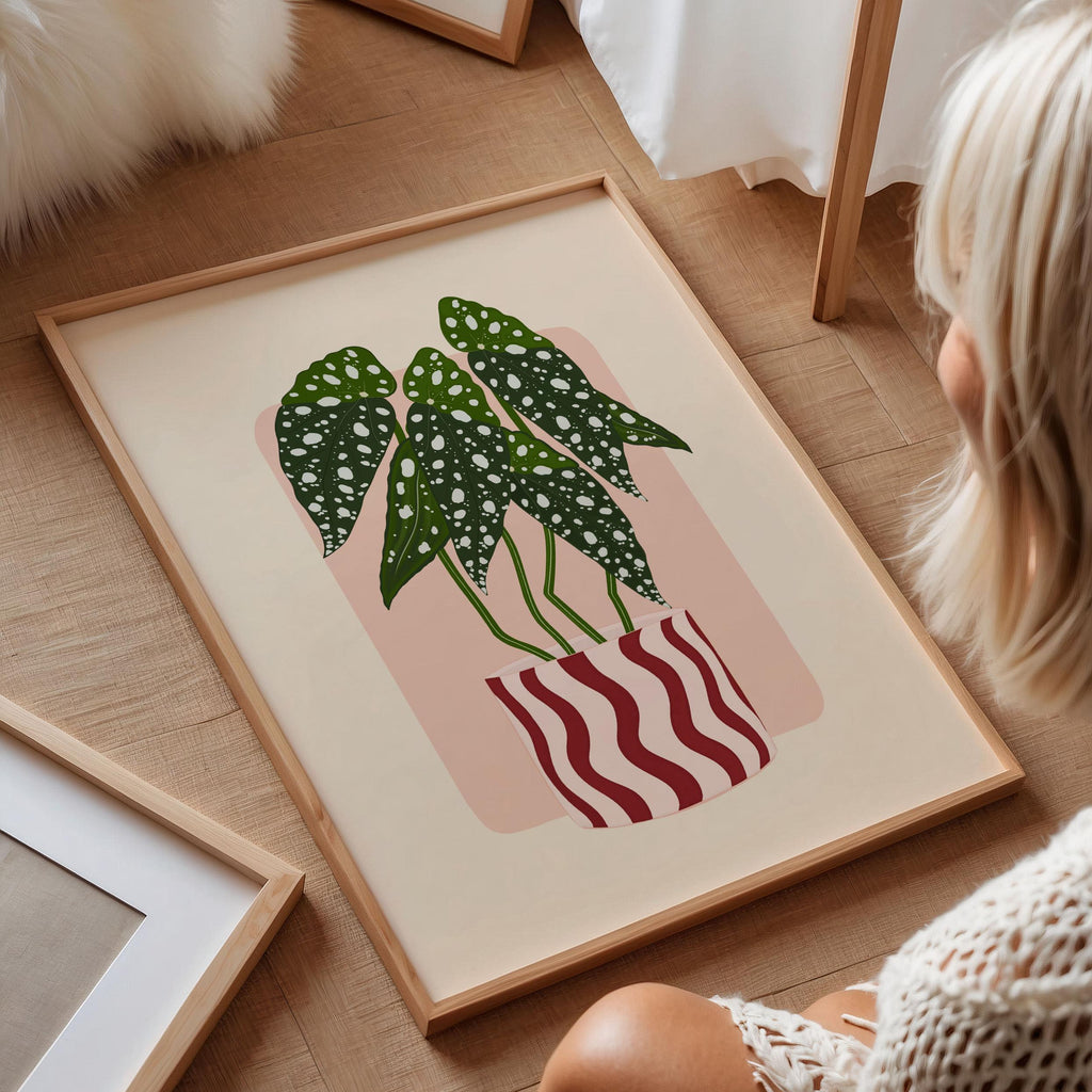 Framed artwork of a plant with a pink background on a wooden floor.