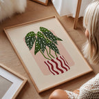 Framed artwork of a plant with a pink background on a wooden floor.