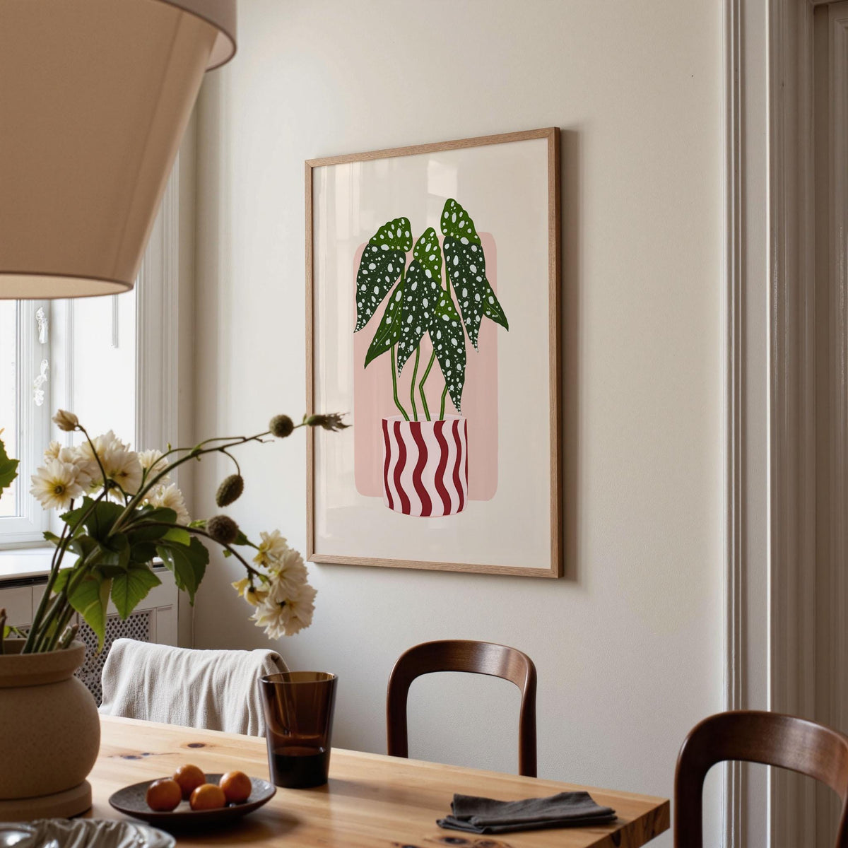 Dining room with a framed plant illustration on the wall, table with flowers and fruit, and chairs.