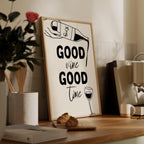Framed poster with 'Good wine Good time' text on a wooden shelf with books and a plant.