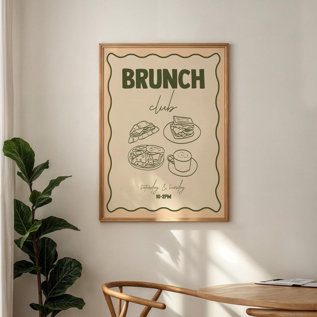 Framed poster with 'Brunch Club' design on a wall with a plant and table in the foreground.