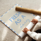 Person unrolling a large sheet of paper with 'Fresh as a daisy' text on a carpeted floor.