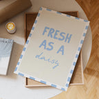 Card with 'Fresh as a daisy' text on a table with a cup of coffee and books.