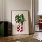 Framed artwork of potted plants on a wall in a room with a green bookshelf and wooden floor.