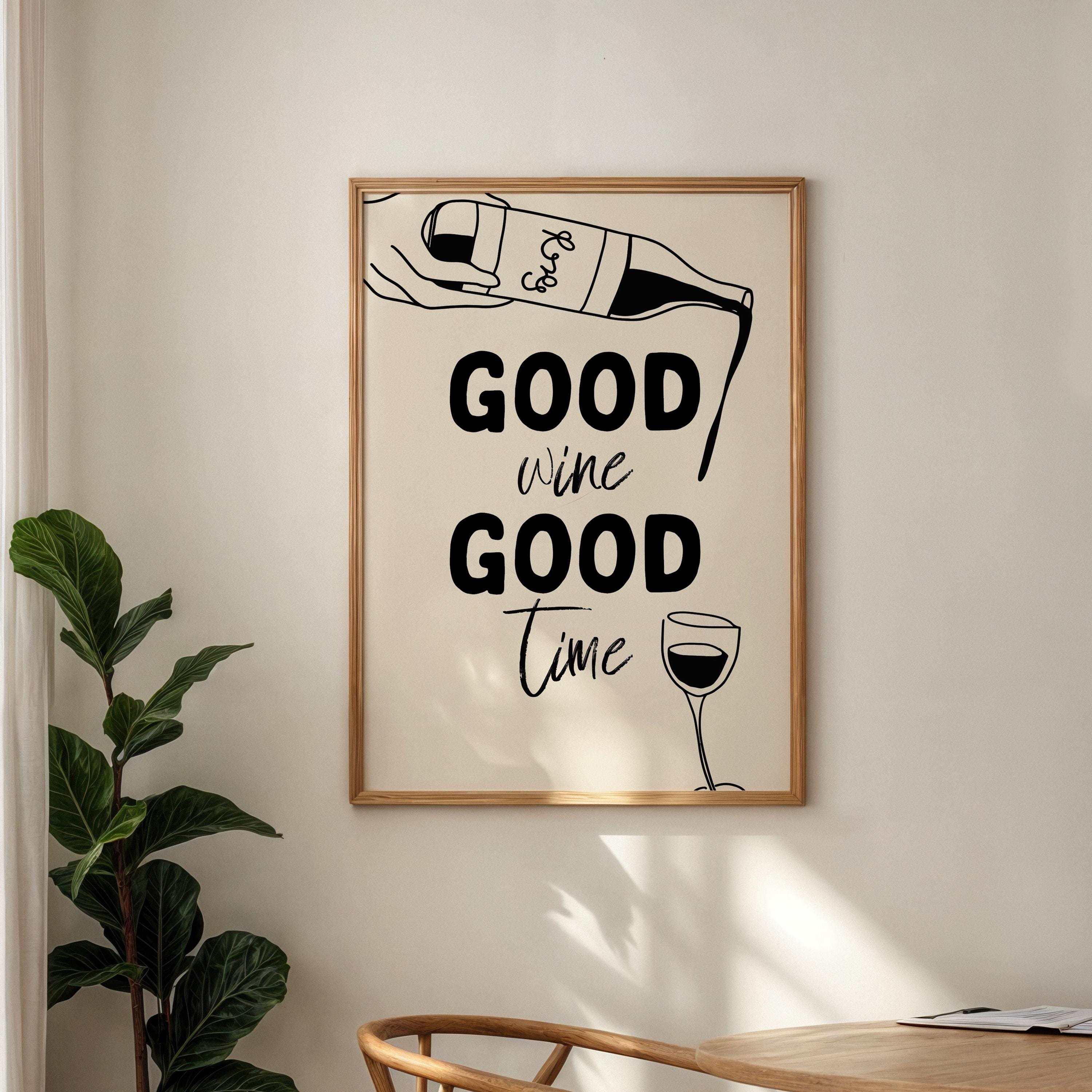 Framed artwork with 'Good wine Good time' text on a wall with a plant and table.
