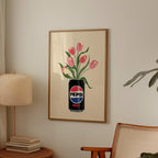 Framed artwork of pink tulips in a Pepsi Max can on a wall with a lamp and chair in the background.