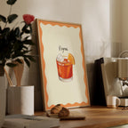 Framed cocktail illustration on a wooden shelf with coffee and books.