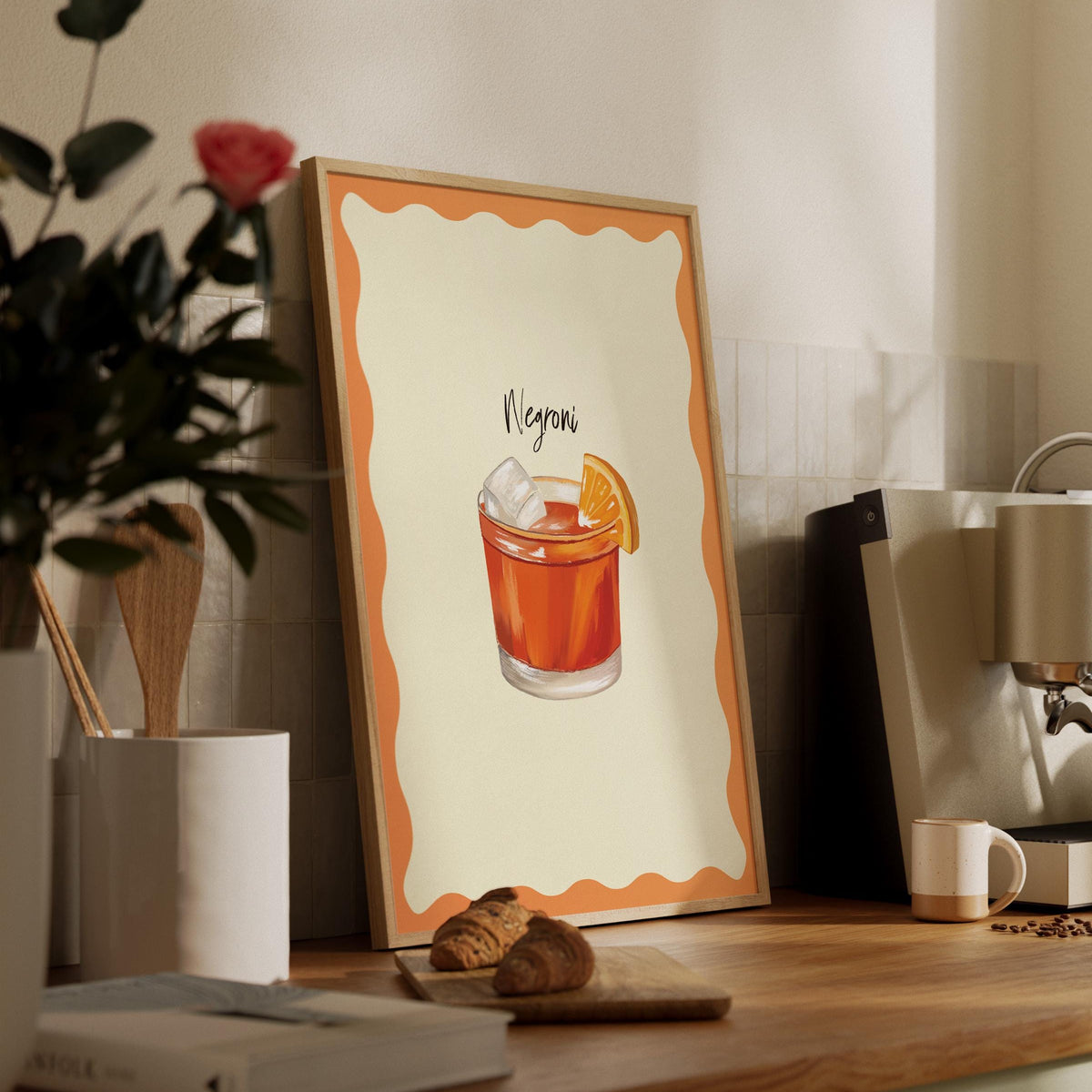 Framed cocktail illustration on a wooden shelf with coffee and books.