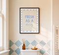 Framed artwork with 'Fresh as a daisy' text on a wall with geometric tile pattern.