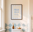Framed artwork with 'Fresh as a daisy' text on a wall with geometric tile pattern.