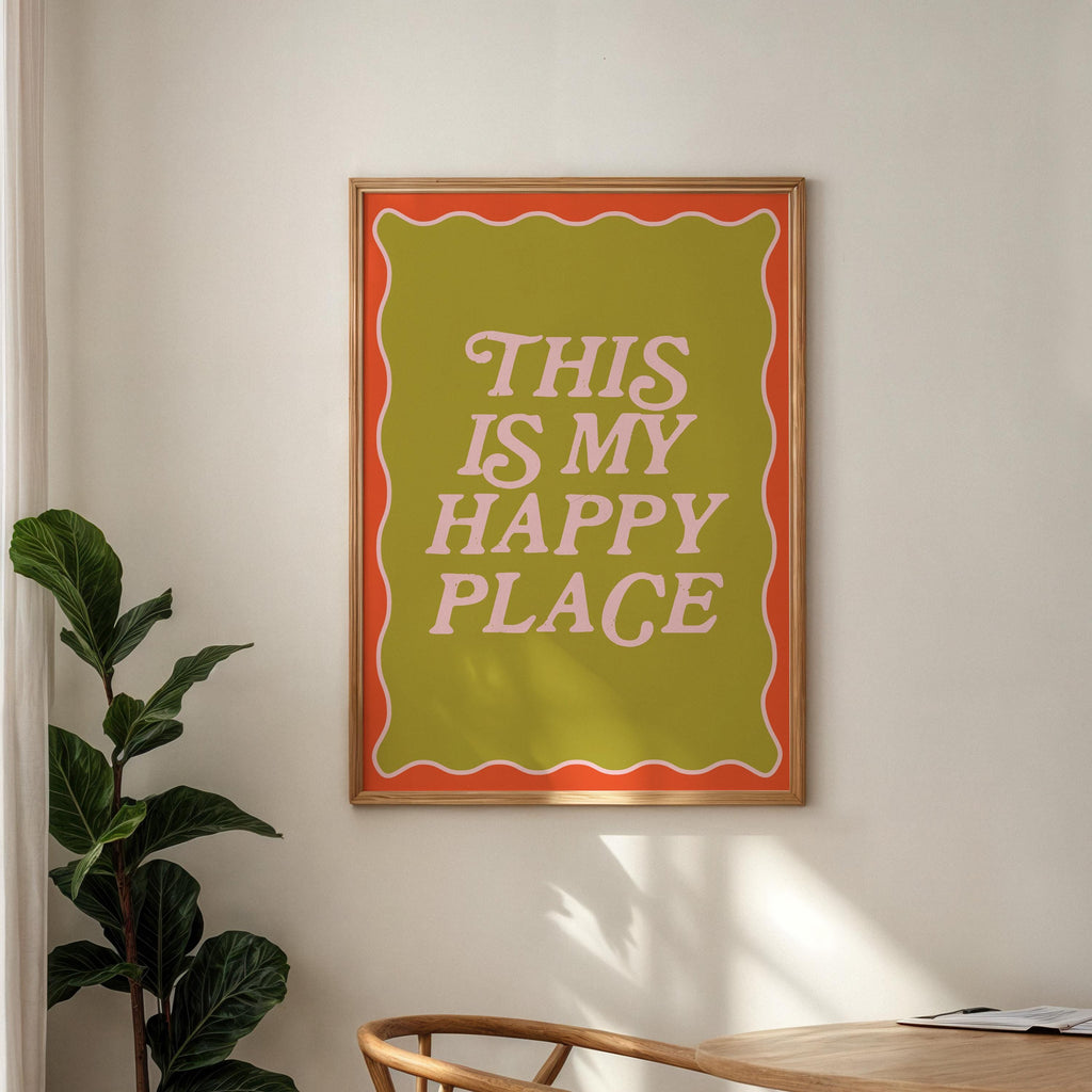 Framed poster with 'This is my happy place' text on a wall with a plant and table in the foreground.
