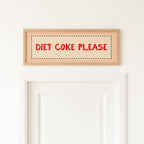Wooden sign with 'Diet Coke Please' text on a white wall above a door.