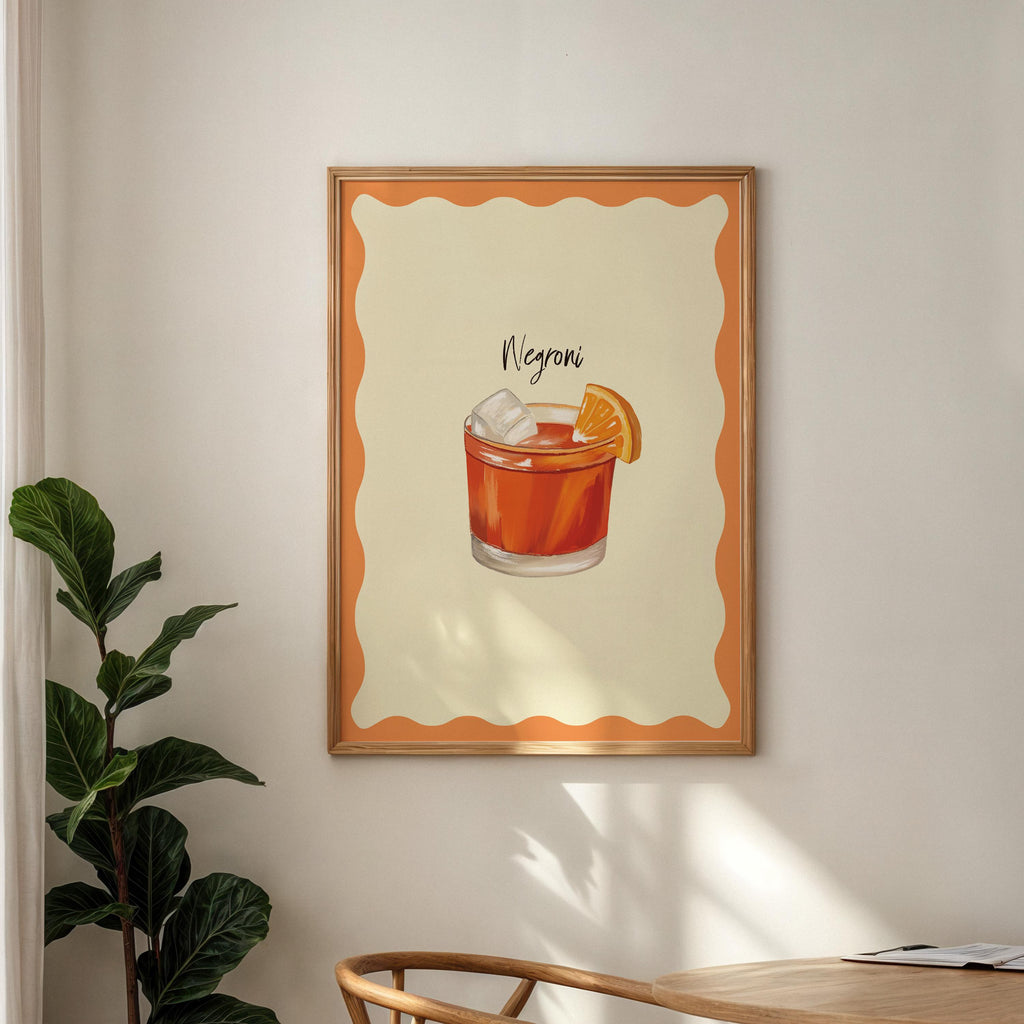 Framed artwork of a Negroni cocktail on a wall with a plant and table in the foreground.