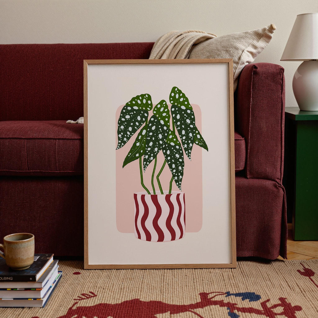 Framed artwork of a potted plant in a living room setting with a red couch and lamp.