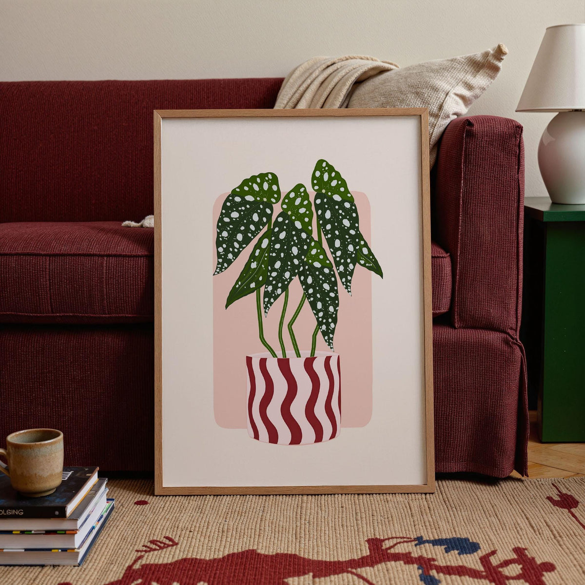 Framed artwork of a potted plant in a living room setting with a red couch and lamp.