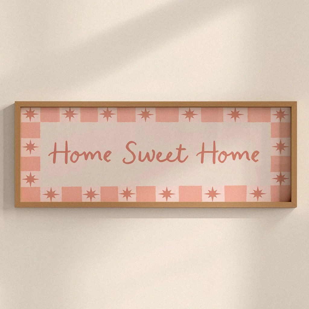 Framed decorative sign with 'Home Sweet Home' text on a checkered pattern against a beige wall.