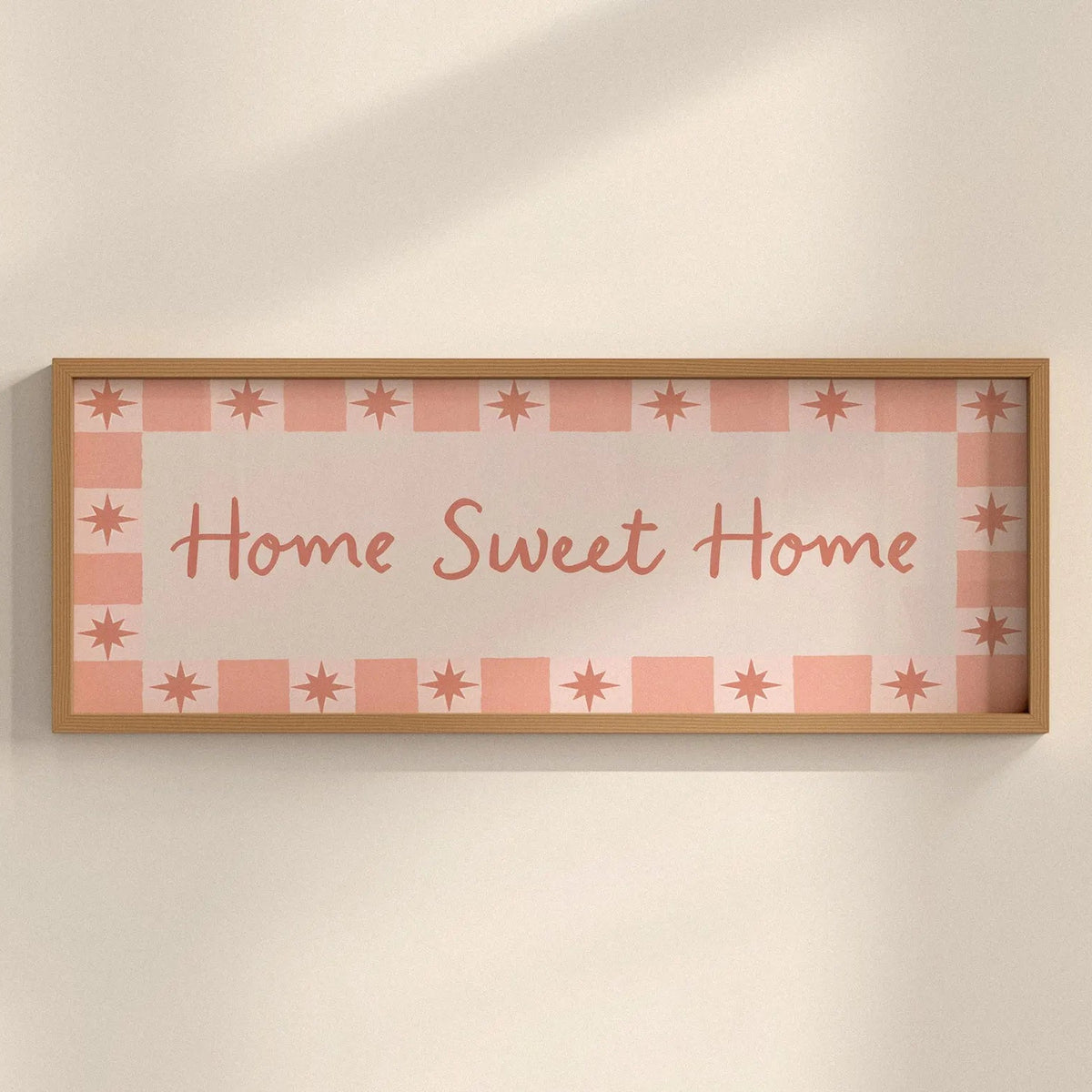 Framed decorative sign with 'Home Sweet Home' text on a checkered pattern against a beige wall.