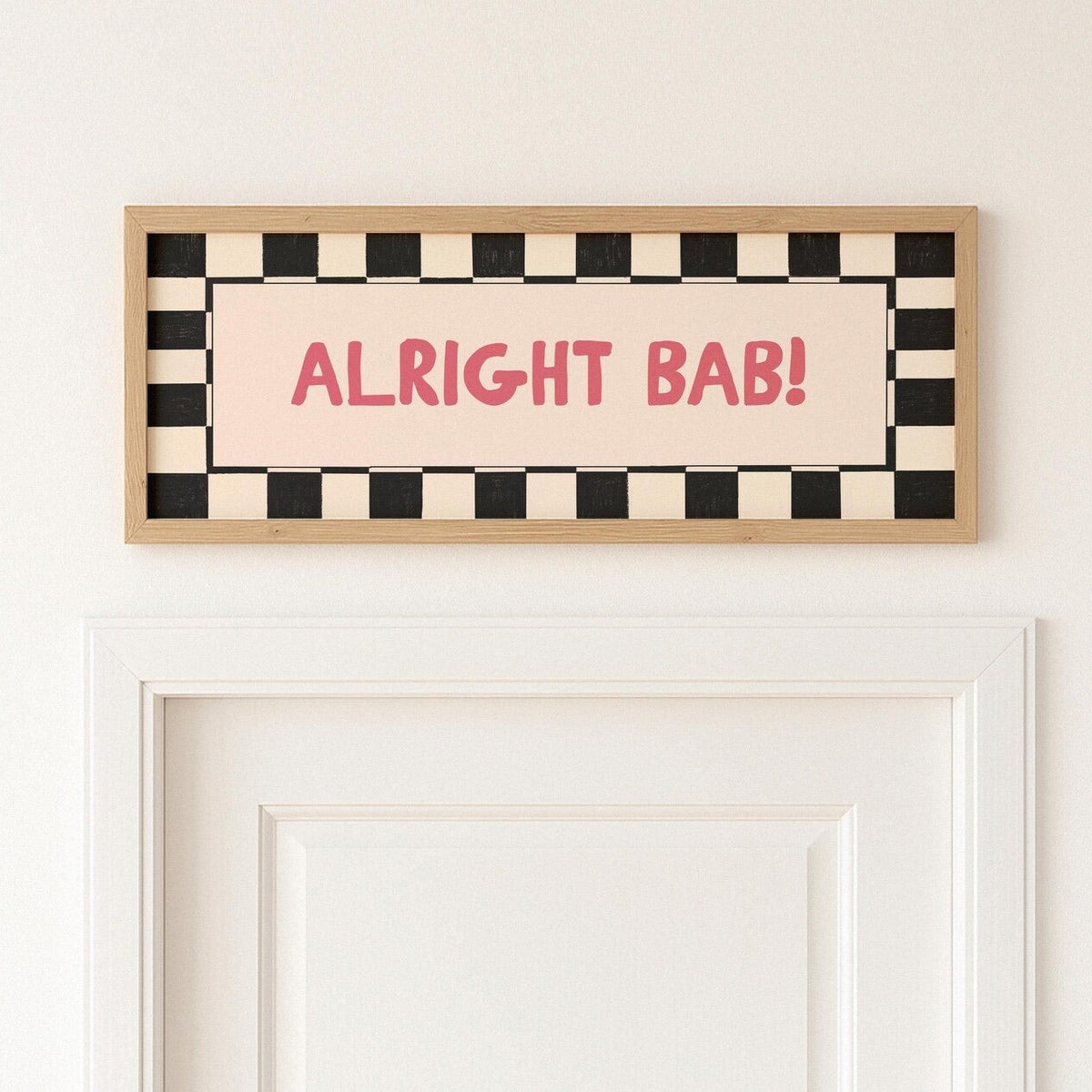 Framed checkered sign with 'ALRIGHT BAB!' text on a white wall.