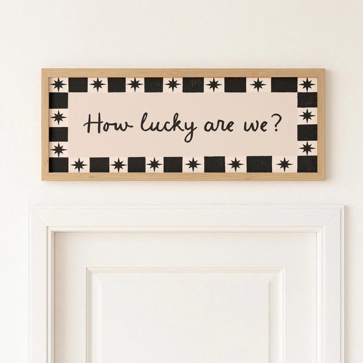 Decorative sign with 'How lucky are we?' text on a white wall.