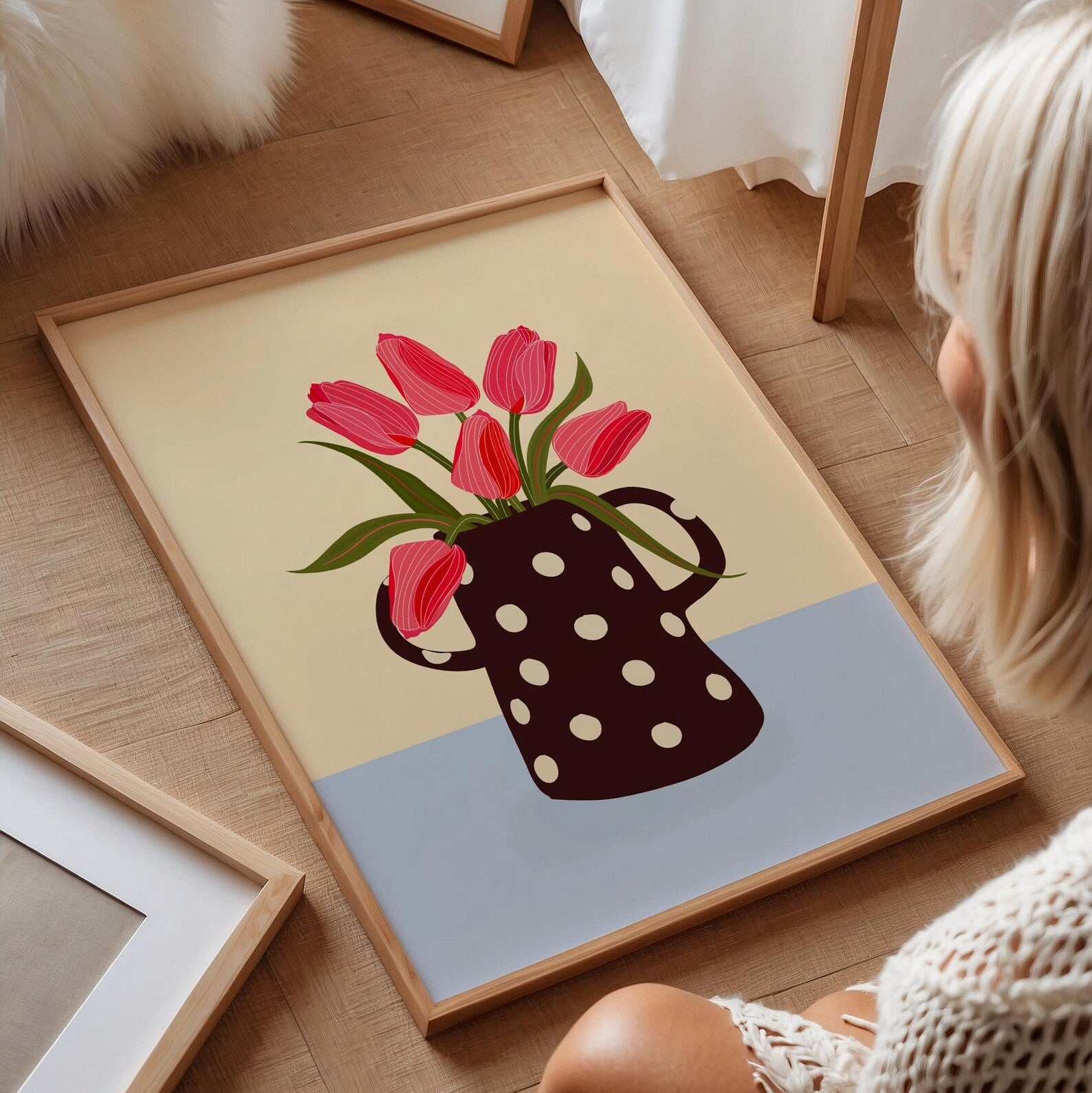 Framed artwork of a polka dot vase with pink flowers on a wooden floor.