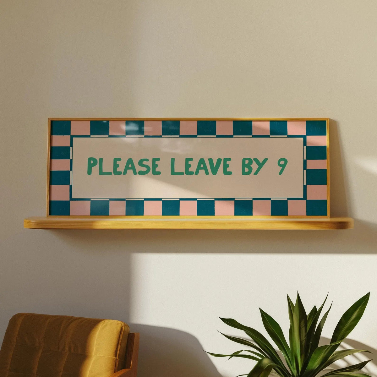 A rectangular wall sign with a wooden frame and a teal and blush pink checkered border, mounted on a beige wall above a wooden shelf. The sign reads 'PLEASE LEAVE BY 9' in teal lettering.