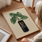 Framed artwork with a plant design and Guinness beer can on a wooden floor.