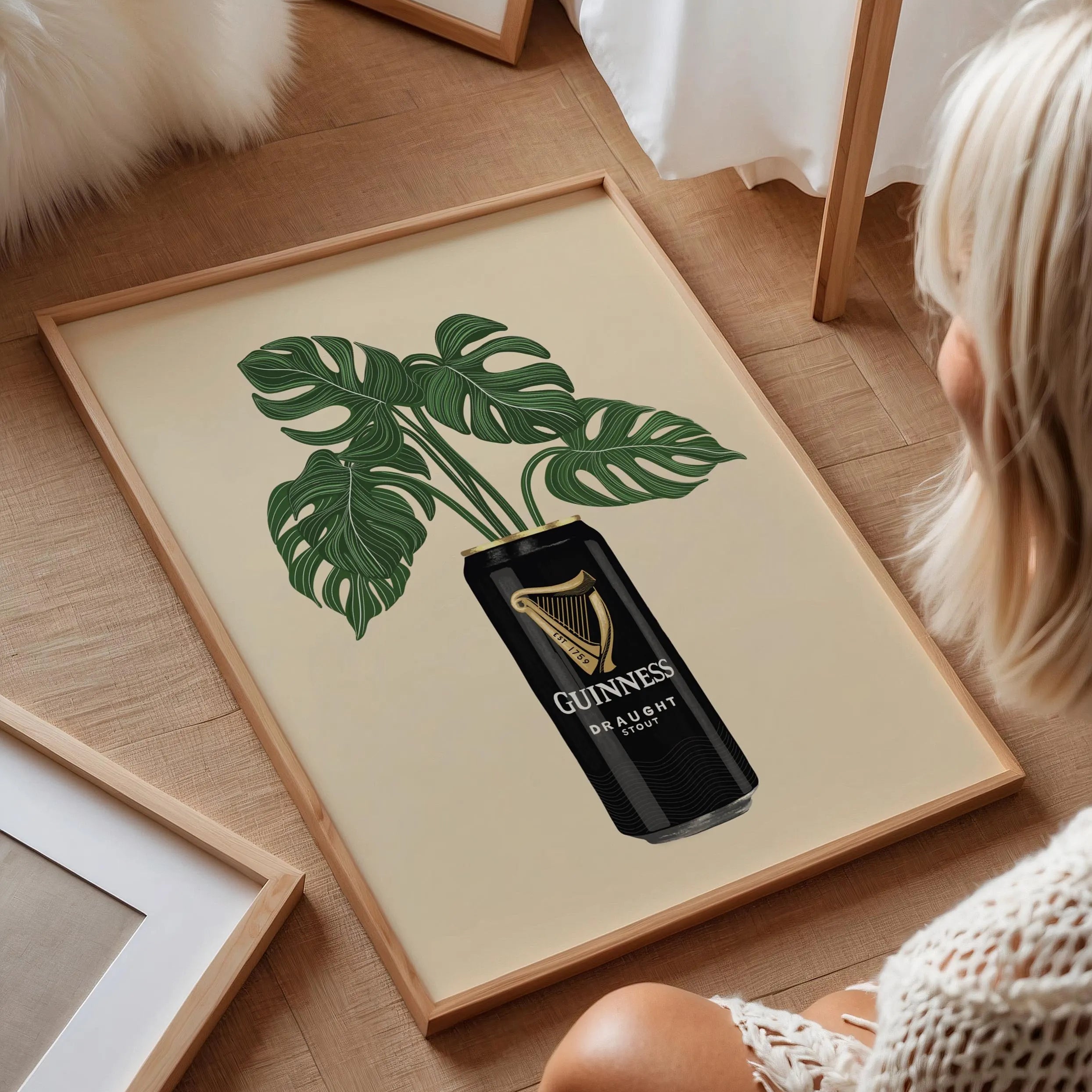Framed artwork with a plant design and Guinness beer can on a wooden floor.