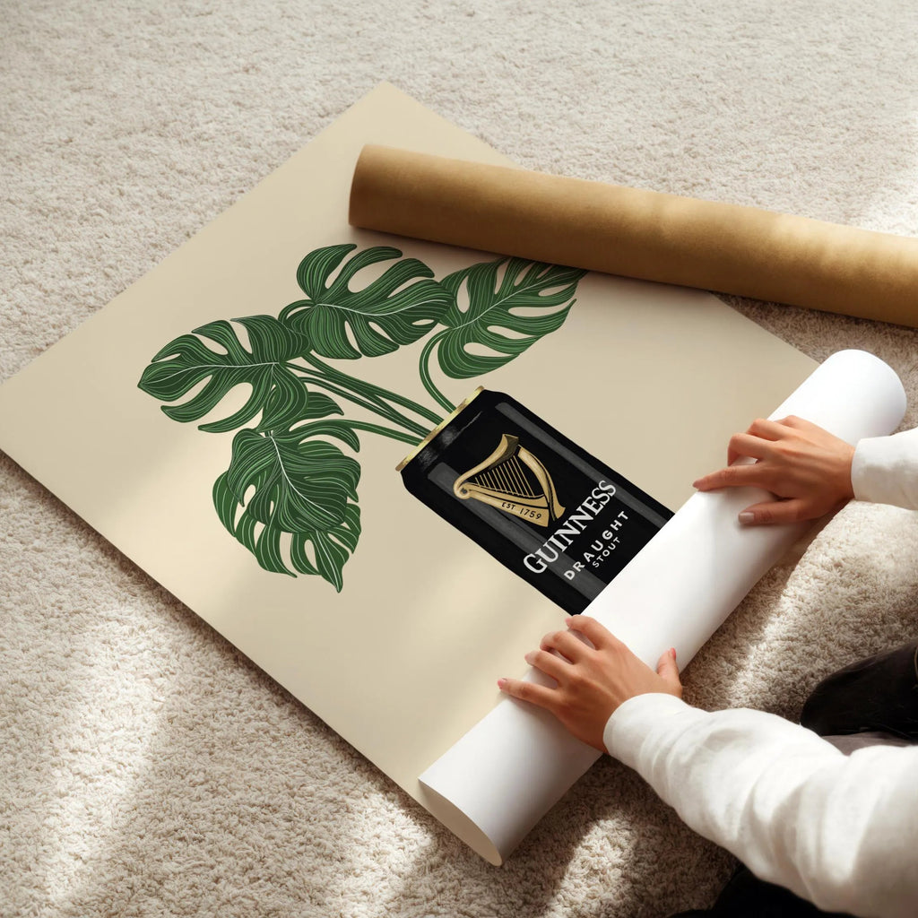 Person unrolling a large paper with a plant design and Guinness bottle graphic on a carpeted floor.